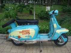 a blue scooter parked on the sidewalk in front of some bushes and trees