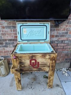 an old cooler sitting on the sidewalk next to a brick wall with a tv above it