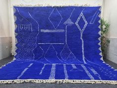 a blue rug with white lines on it and fringes hanging from the sides, in front of a wall