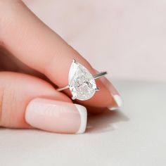 a woman's hand holding a ring with a pear shaped diamond on top of it