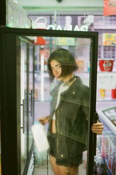 a woman standing in front of a store window with her hand on the door handle