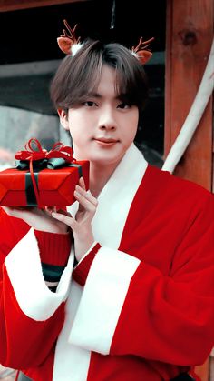 a man in a red and white outfit holding a present box with reindeer antlers on it