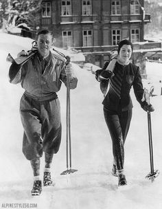 black and white photograph of two people on skis in front of a lodge building