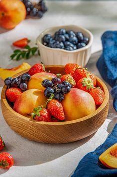 a wooden bowl filled with fruit next to blueberries and peaches on top of a table