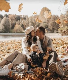 a man and woman sitting on the ground with a baby in their lap, surrounded by leaves