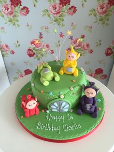 a green birthday cake with three cartoon characters on it and flowers in the back ground