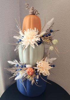 a blue pumpkin decorated with white flowers and feathers on top of a black round table