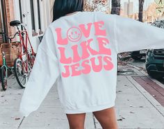 a woman walking down the street wearing a sweatshirt that says love like jesus