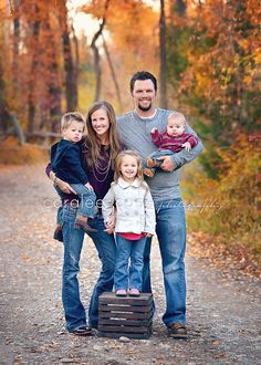 a family posing for a photo in the woods with fall foliage and trees behind them