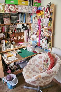 a chair and desk in a room with lots of clutter on the shelves above it