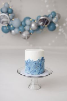 a blue and white cake sitting on top of a glass plate next to some balloons