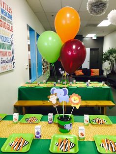 an office decorated with green and yellow table cloths, plates, and colorful balloons