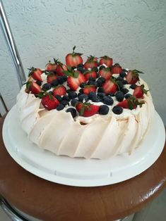 a white cake with strawberries and blueberries on top sitting on a wooden table