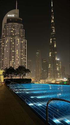 an empty swimming pool in the middle of a city with skyscrapers lit up at night