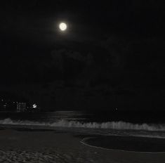 a full moon is seen over the ocean on a dark night with waves coming in