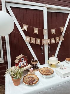 This photo contains a variety of pies and cupcakes as well as 2 white cakes across a white table as well as mini animal figures such as a pig, horse, cow, rooster, and a farm house to tie it all together. There are also balloons the color white, red and cow print on both ends of the table. Farm Birthday Party Aesthetic, Modern Farm Theme Birthday, Vintage Farm Birthday Party, Neutral Farm Birthday Party, Minimalist Farm Birthday Party, Neutral Barnyard Birthday, Farm Theme Centerpieces, Barnyard Dance Birthday Party