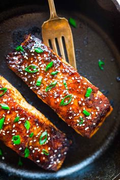 two salmon fillets in a skillet with sesame seeds and green onions on top