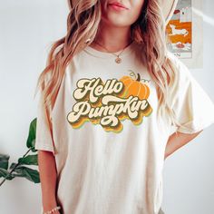 "Hello Pumpkin Shirt, Womens Fall Shirts, Fall Tshirt, Retro Fall Graphic Tees, Vintage Inspired T shirts, Autumn Tshirts, Pumpkin Tee Shirt Our Hello Pumpkin shirt makes the perfect addition to your fall collection - also makes a great gift! How we make our shirts - This shirt is made with a professional DTG Printing machine. Printed with eco-friendly water based inks that prints the image/designs on the shirt allowing the image to become part of the shirt so there is no peeling or cracking ove Retro Fall T-shirt With Screen Print, Retro Yellow T-shirt With Slogan, Yellow T-shirt With Screen Print For Fall, Retro Screen Print T-shirt For Fall, Short Sleeve T-shirt With Screen Print For Fall, Retro Slogan T-shirt For Fall, Retro Cotton Shirt With Text Print, Retro Cotton Top With Letter Print, Casual Yellow T-shirt For Fall