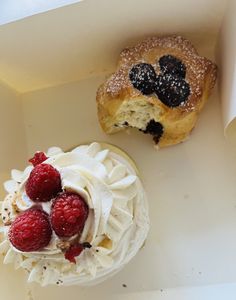 two pastries in a box with raspberries and cream on the top one