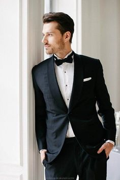 a man in a tuxedo leaning against a wall