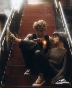 two people sitting on the stairs holding a lit candle and looking at each other's eyes