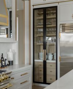 a kitchen with white cabinets and gold trim on the glass doors, along with an open refrigerator