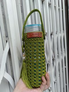 a hand holding a green crocheted purse with a water bottle in the pocket