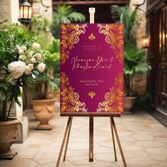 an easel with a wedding card on it in front of some potted plants