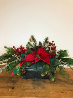 a christmas arrangement with poinsettis and greenery in a black box on a wooden table