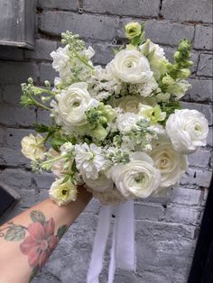 a bouquet of white flowers is held up against a brick wall