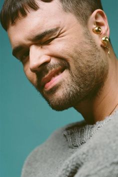 a close up of a person with a beard and piercings on his ear wearing a sweater