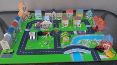 a toy town with cars, trucks and buildings on the road that runs through it