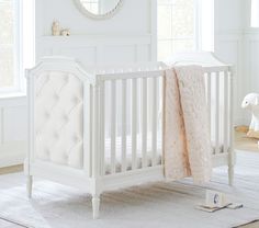 a white baby crib with a pink blanket on the bed and a teddy bear next to it