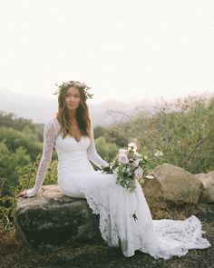 a beautiful woman sitting on top of a rock with flowers in her hair and wearing a wedding dress