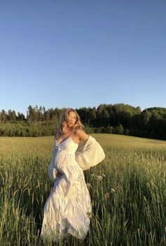 a woman in a white dress is standing in the middle of a field with her arms behind her head