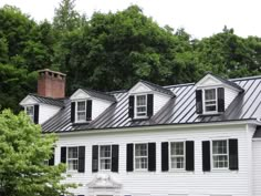 a large white house with black shutters on the front and side windows, surrounded by trees