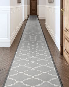 a long hallway with white walls and wooden doors leading to an open door on the other side