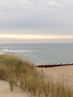 an empty beach with waves coming in from the water and grass growing on the sand