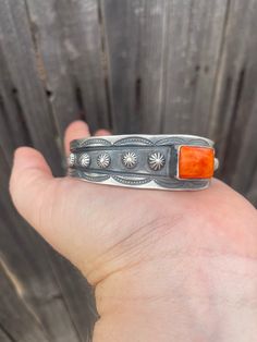 a hand holding an orange stone and silver ring on it's fingers with wood background