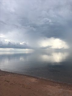 the sky is very cloudy and there are clouds in the distance over the water on the beach