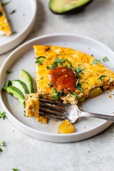 a slice of quiche on a white plate with a fork and avocado