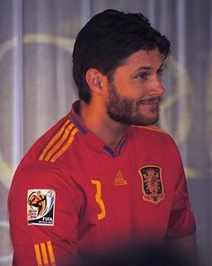 a man with a beard wearing a red shirt and smiling at someone in front of him