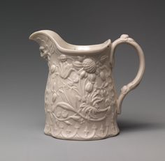 a cream colored pitcher with floral designs on the outside and inside, sitting on a gray surface