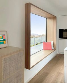 a kitchen with white cabinets and an open window that looks out onto the water outside