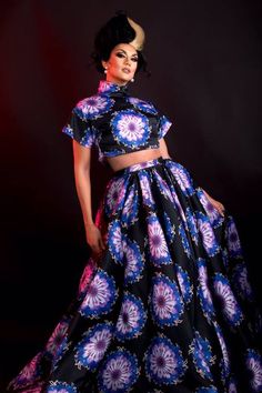 a woman in a blue and purple dress standing on a black background with her hands on her hips