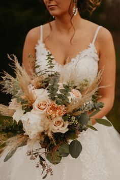 a woman in a wedding dress holding a bridal bouquet with flowers and greenery