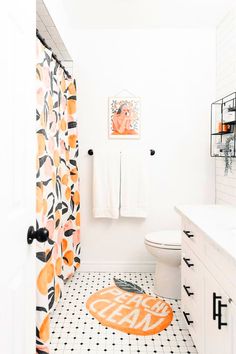 a white bathroom with orange and black decor on the shower curtain, toilet seat cover and rug