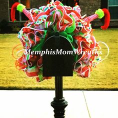 a colorful wreath on top of a mailbox in front of a house with red, green and white streamers