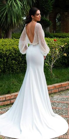 a woman in a white wedding dress is standing on a brick walkway with her back to the camera