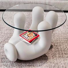 a glass coffee table with a book on it's legs and a magazine in the shape of a hand